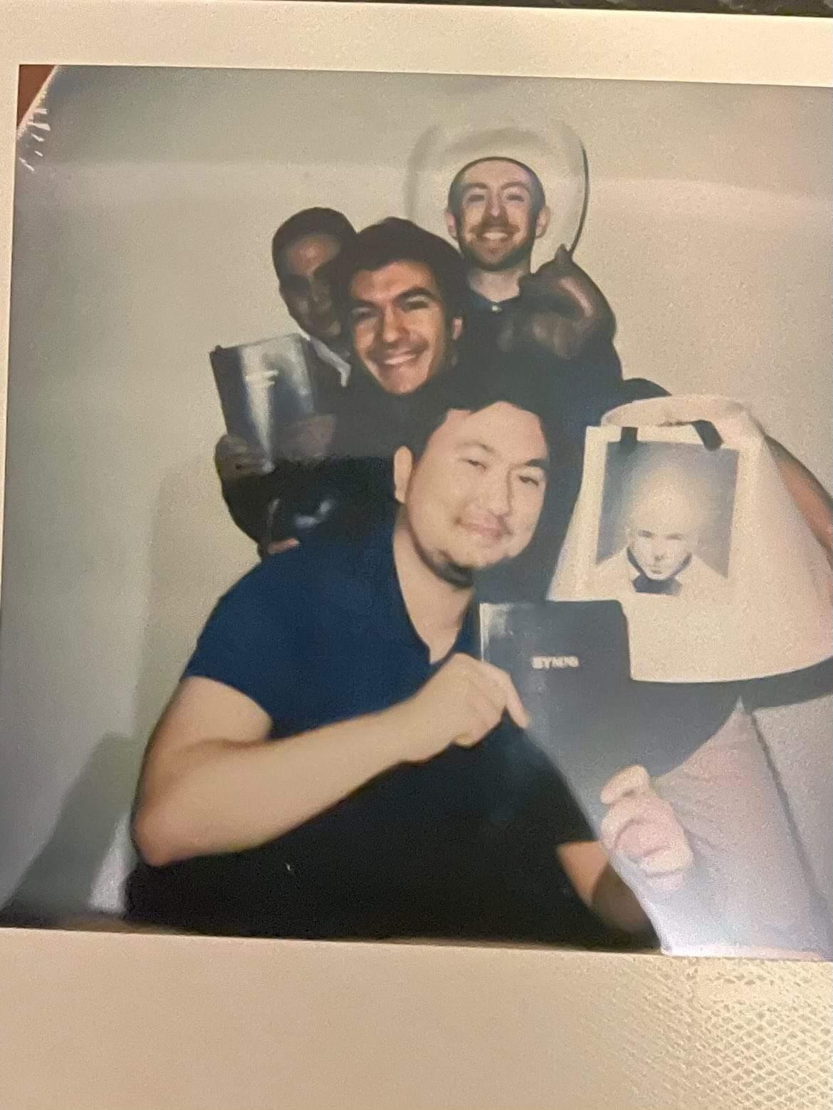 A blurry polaroid of UCDC Fellow Andrew Neciuk and three friends holding books and other items 