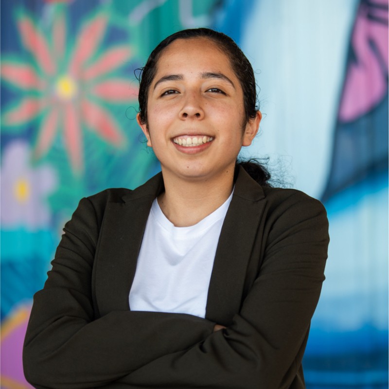 young latina college student smiling with her arms folded wearing a dark blazer and white shirt