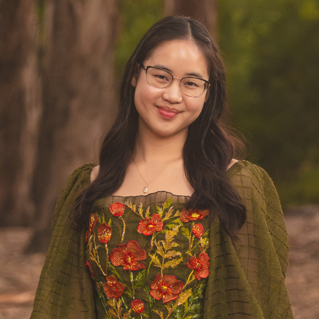 young woman in glasses and a green patterned dress in front of greenery