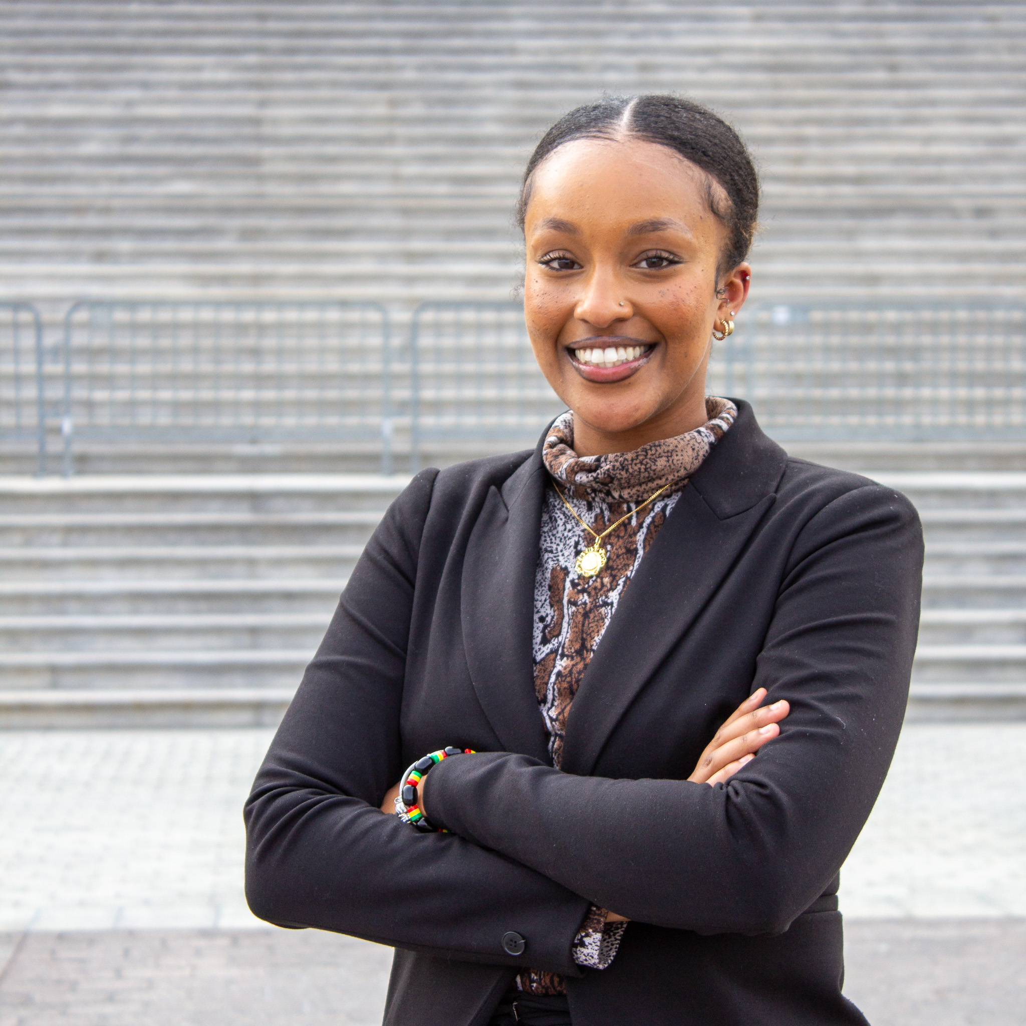 young Habesha woman smiling with arms crossed wearing a black blazer and a brown, black, and white animal print turtleneck