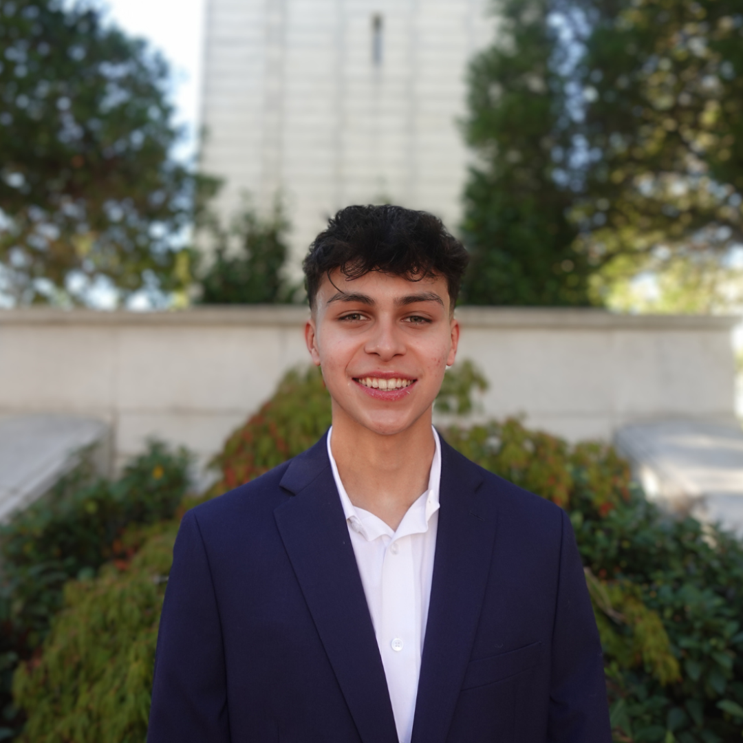 young man in front of campanile in navy blue blazer and white button-up