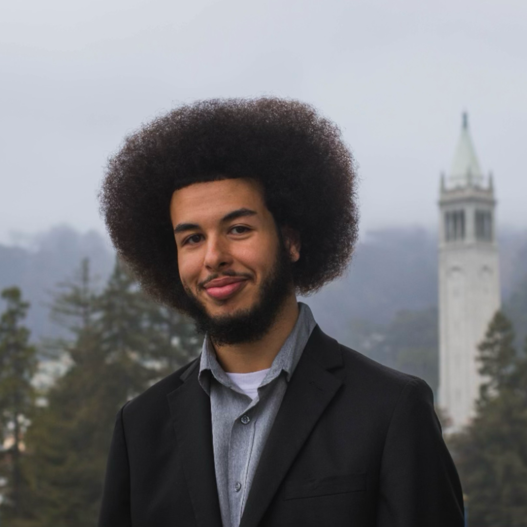 young man in front of Berkeley campanile in black suit and gray button-up shirt