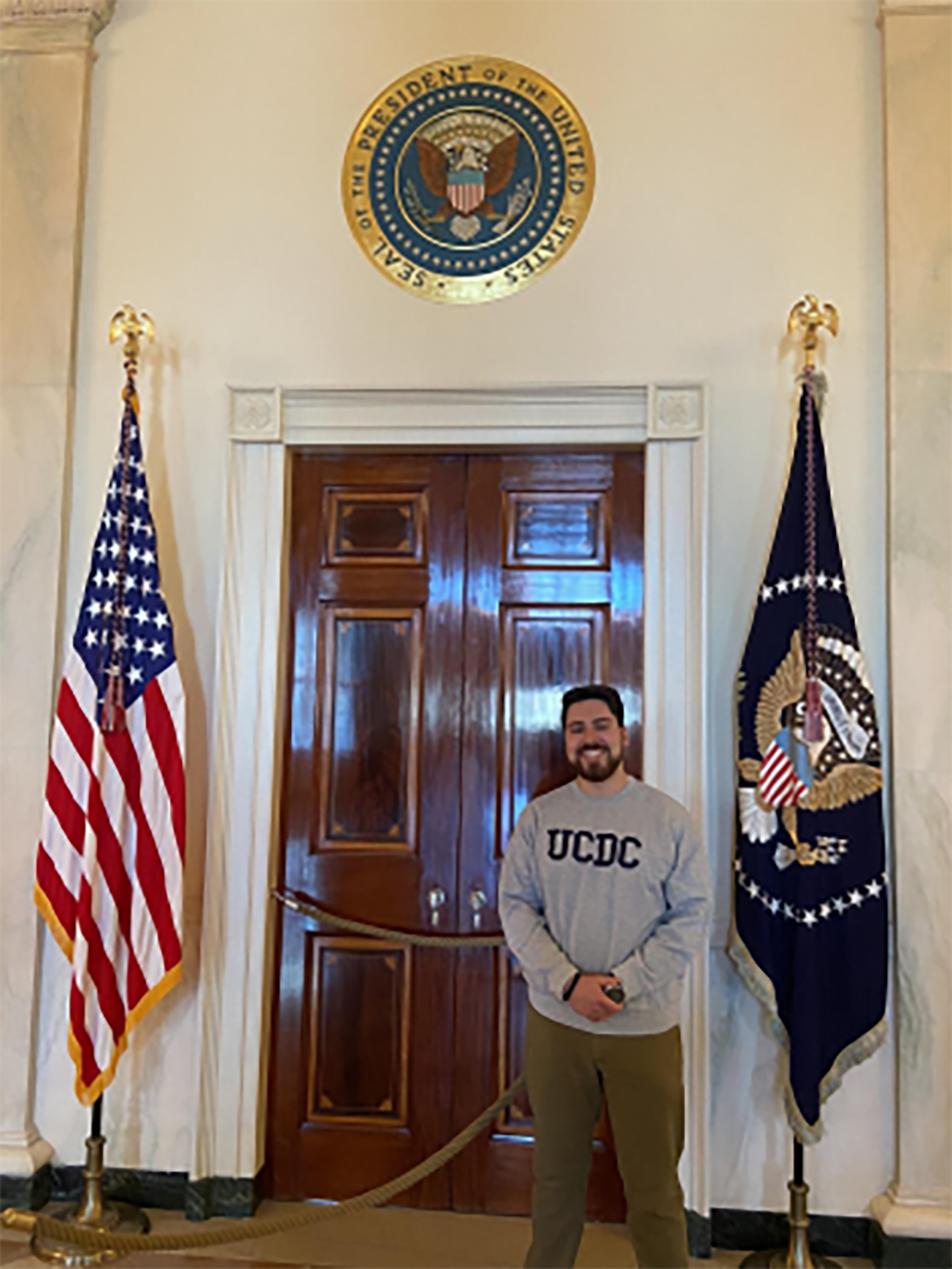 Spring 2023 UCDC Fellow Nathan Jauregui standing in front of a door with the seal of the US President
