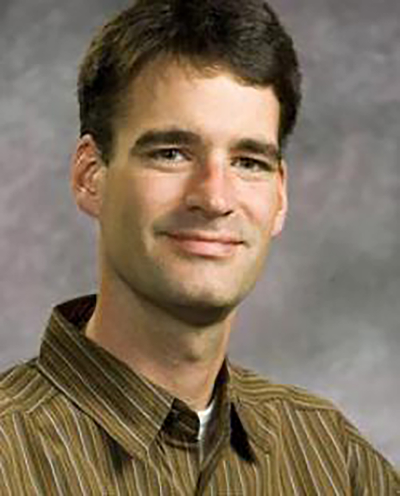 Robert Van Houweling, wearing a brown striped buttondown against a gray background
