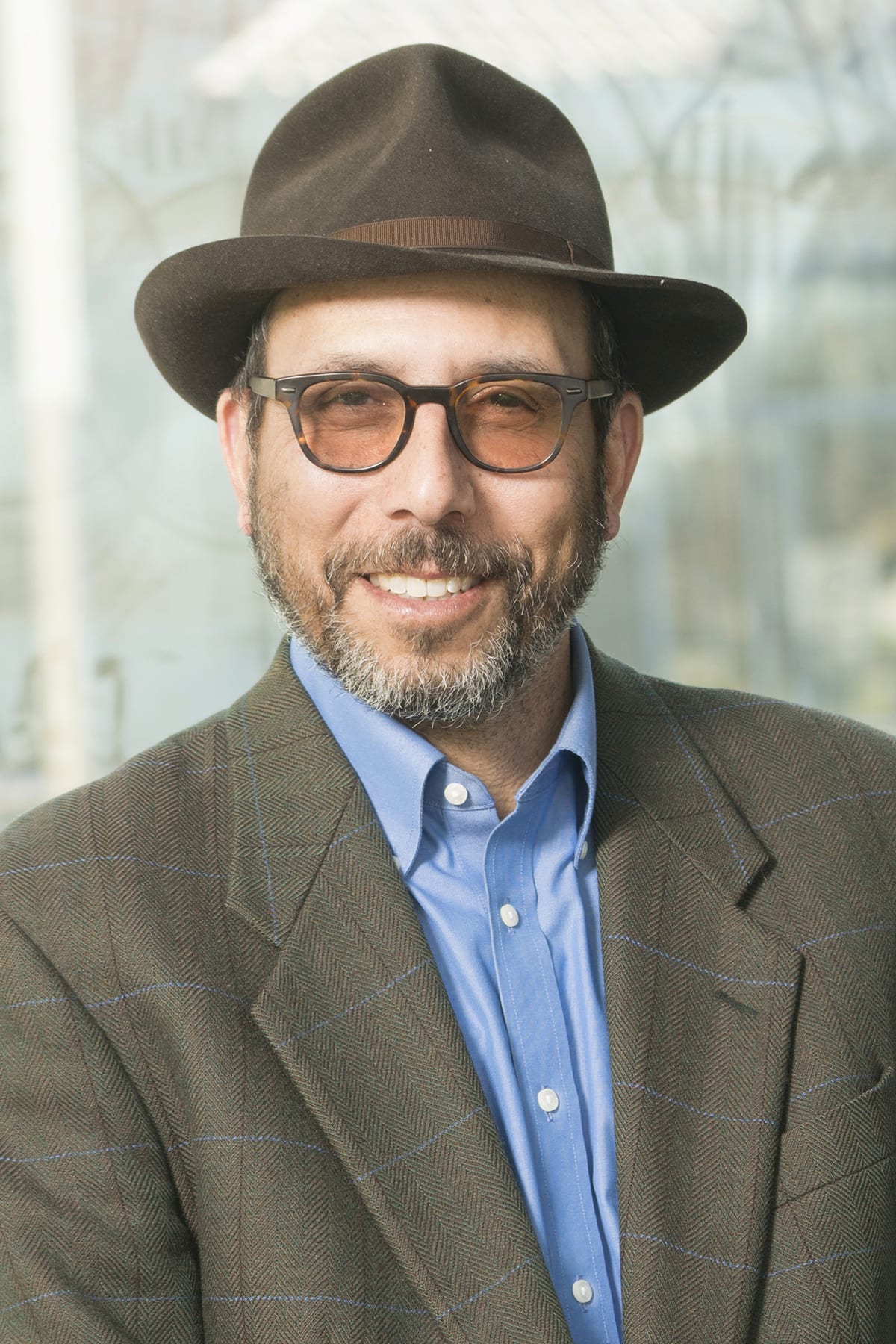 Johnathan Simon smiling in a fedora, brownish-green suit and blue shirt