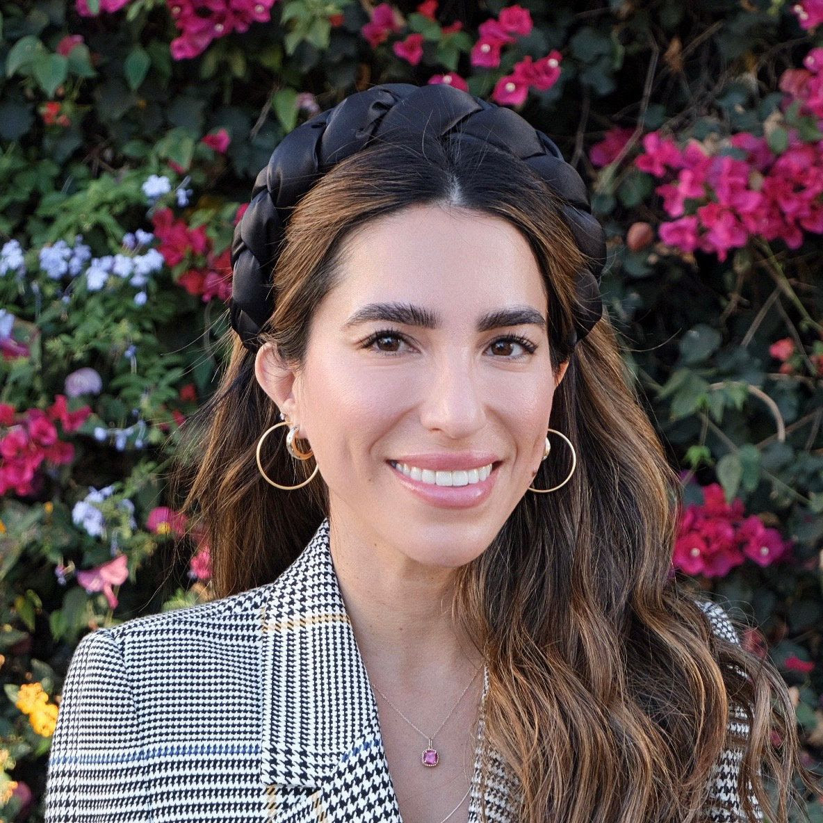 stephanie canizales long brown haired woman smiling in front of flower bush