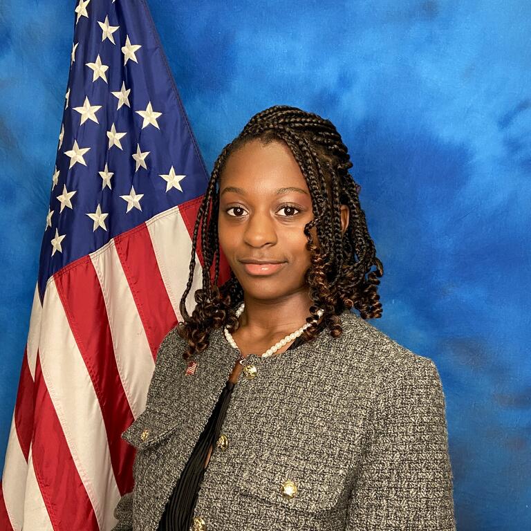 Black young woman stands in front of American flag for a professional photo