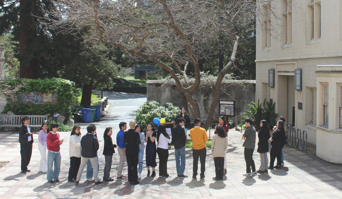 A group of about 20 people standing together outside during the day in a courtyard