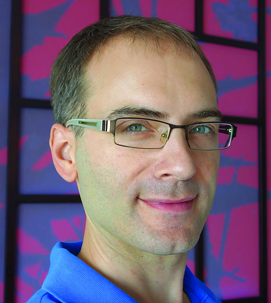Gabriel Lenz from neck up in a blue collared shirt against a patterned pink and purple background