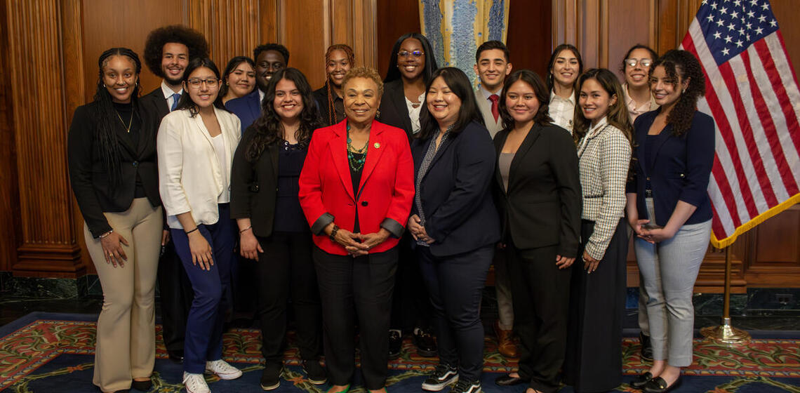 A group of people in professional clothing pose with Congresswoman Barbara Lee in a stately interior room