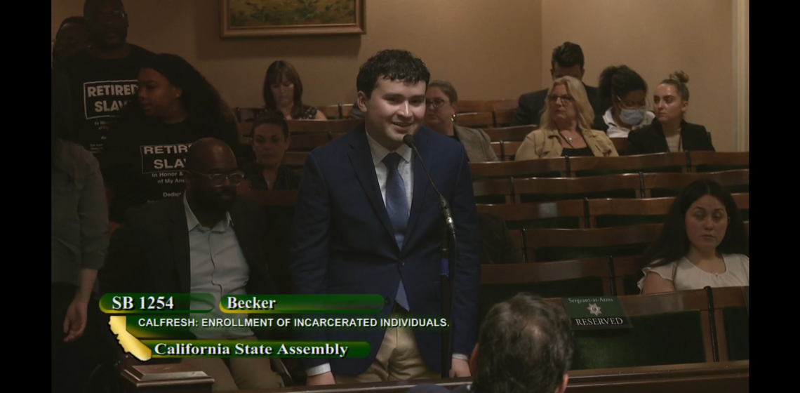 A young man in a suit gives testimony before a legislative body
