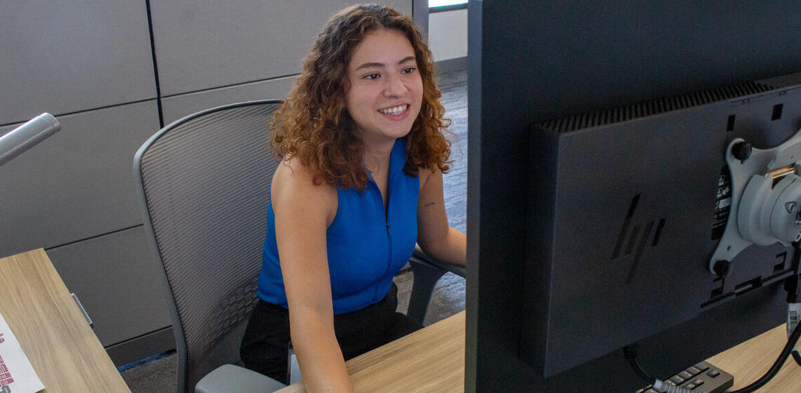 A young woman in professional clothing works at a desktop computer