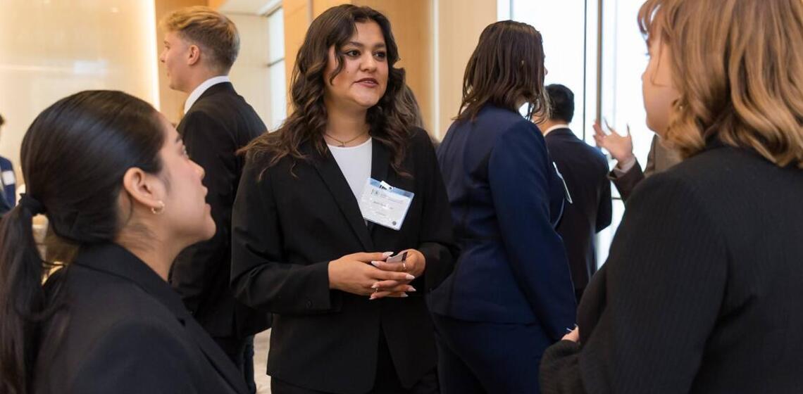 A young women in professional clothing speaking to others also in professional clothing in an interior space