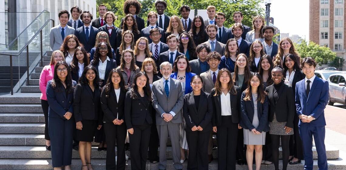 A group of 51 people in professional clothing pose on stairs outside on a sunny day