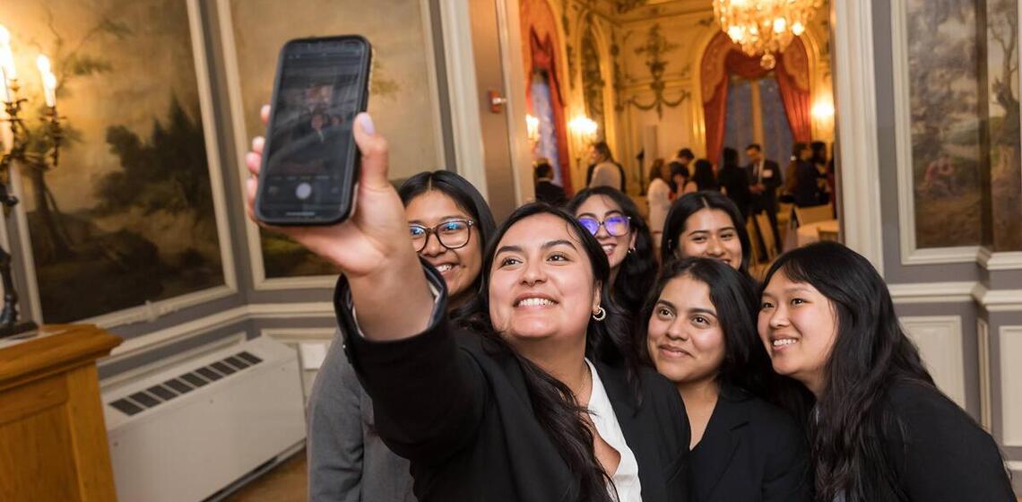 A group of young people in professional clothing post for a selfie in a formal interior space