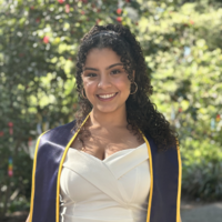 young latina woman smiling in white dress and blue and yellow UC Berkeley graduation stole with curly shoulder length hair