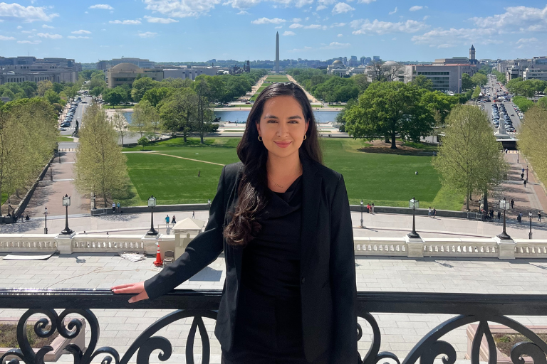 young latina woman standing on the balcony of the U.S. capitol with the Washington Monument behind her